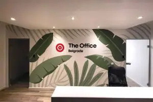 Mural sa tropskim listovima i logotipom firme The Office Belgrade – oslikan zid na ulazu.