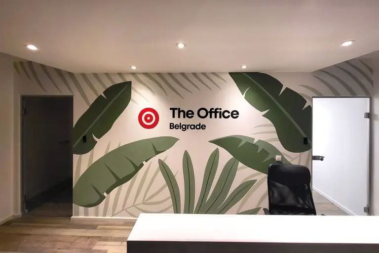Mural sa tropskim listovima i logotipom firme The Office Belgrade – oslikan zid na ulazu.