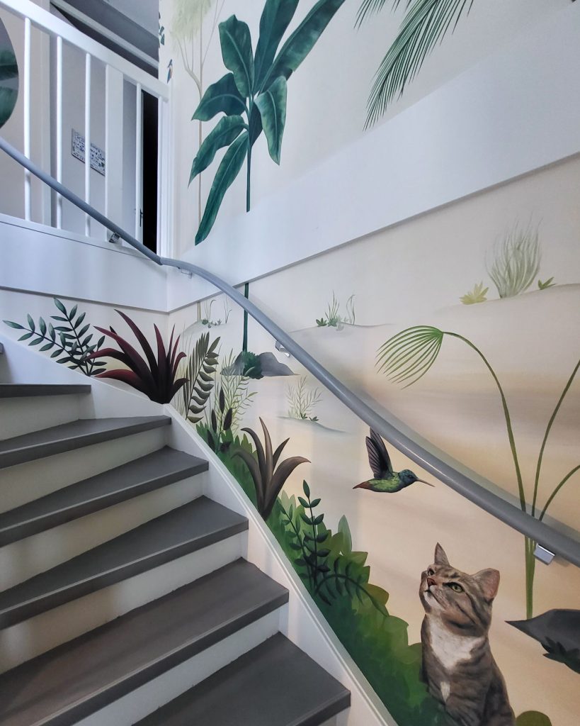 Mural sa tropskim biljkama, mačkom i kolibrijem koji prati zid stepeništa