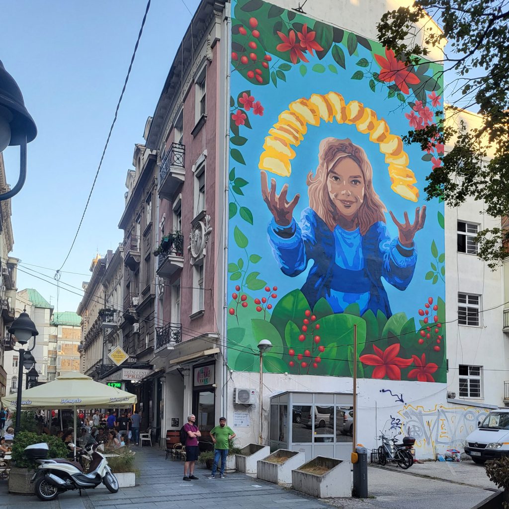 Reklamni mural na fasadi zgrade u centru Beograda, prikazan u kontekstu ulice