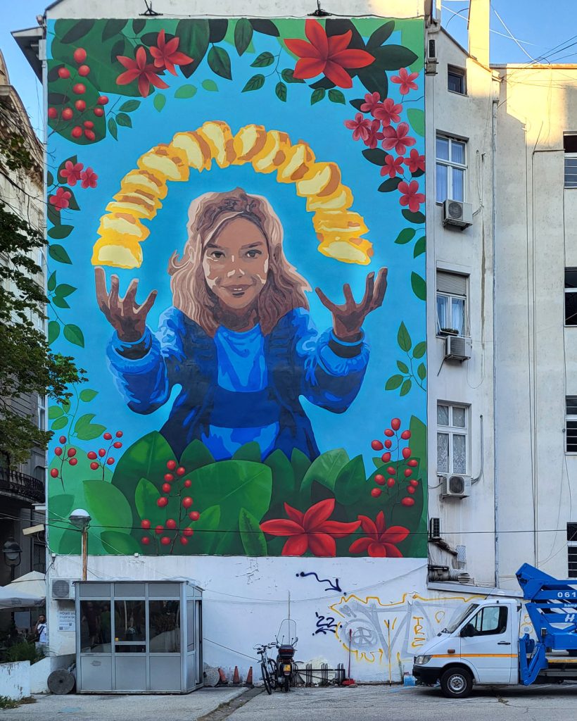 Veliki reklamni mural sa ilustracijom devojke, cveća i čipsa na fasadi u Beogradu
